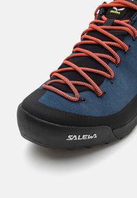 Blå og svart klatresko med en teksturert overdel, med oransje snøring og en gummisåle. SALEWA-logoen er synlig på siden.