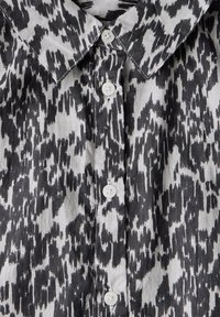 Zwart-wit gemusterd shirt met een puntige kraag, vijf witte knopen en een textiele stof met een dynamisch, abstract patroon.