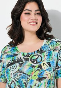 Camiseta de manga corta y corte holgado con un estampado gráfico colorido que presenta varios patrones, incluidos símbolos de paz y globos terráqueos, sobre un fondo claro.