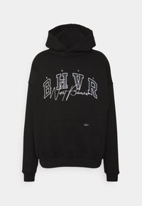 Černá mikina s kapucí a přední kapsou, na které je bíle a šedě potištěný text: "BHVR Worst Behavior" ve výrazném písmu. Měkká látka, oversized střih.
