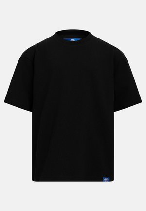 Schwarzes T-Shirt mit kurzen Ärmeln und Rundhalsausschnitt, mit einem kleinen blauen Etikett mit der Aufschrift "REBEL" am unteren Saum vor neutralem Hintergrund.
