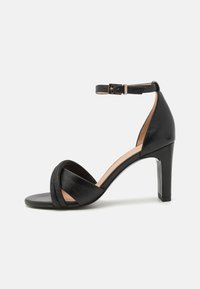 Schwarze High Heels Sandale mit einem strukturierten vorderen Riemen, verstellbarer Knöchelriemen und glattem Lederfinish. Offene Zehenpartie.