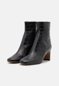 Botas de tobillo de imitación de cuero negro con textura de cocodrilo, puntera afilada y tacón de altura media. Presenta un cierre con cremallera lateral.