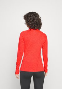 Lange mouw sporttop in gemêleerde felrode stof. Voorzien van een opstaande kraag en een aansluitend ontwerp, met duimgaten aan de mouwuiteinden.