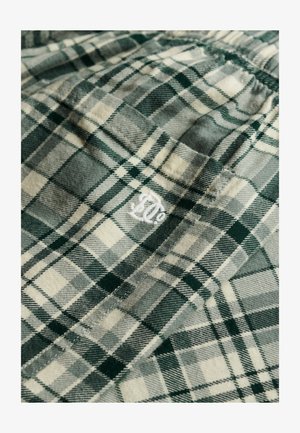 Tkanina flanelowa w kratę w odcieniach zieleni i beżu o teksturowanym wykończeniu. W rogu znajduje się białe haftowane logo.