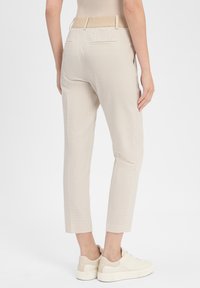 Beige karierte Hose mit glatter Textur, cropped Länge und einem breiten Bund mit dezentem Logodesign. Kombiniert mit weißen Sneakern.