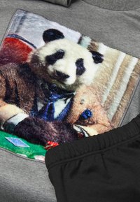 Šedá kratší rukávová košile s chlupatým grafikem pandy v obleku, umístěná na barevném pozadí hracích karet. Černá látka na spodní části.