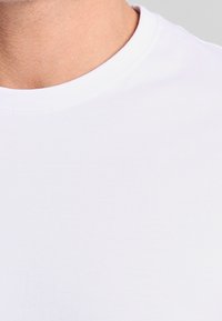 Witte katoenen t-shirt met een ronde halslijn en een gladde textuur, met een aansluitend ontwerp en gelijkmatige stiksels rond de kraag.