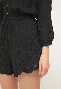 Shorts noirs brodés avec motifs floraux portés avec un haut à manches longues assorti, avec un ourlet festonné et une taille à cordon.