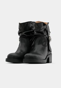 Mustad nahast pahkluusaapad, millel on lahtine disain, ümar varvas ja madal plokkkonts. Küljel on metallist aksentdetail.