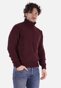 Maglione a collo alto bordeaux in texture lavorata a maglia, con orlo e polsini a coste, abbinato a jeans in denim blu chiaro.