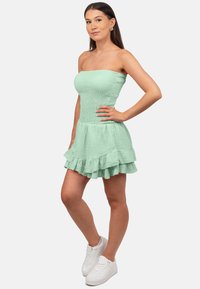 Mintgroene strapless mini-jurk van textuurstof, met een geschulpte onderrand en een getailleerde top, gecombineerd met witte sneakers.