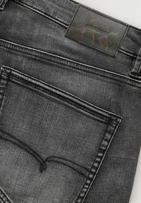 Baglomme på sorte denimjeans med synlige syninger og en mørk lædermærke med teksten "DENIM SUPPLY."