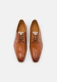 Chaussettes en cuir tan avec une finition polie, pointe pointue, perforations décoratives et lacets noirs. Étiquette de marque visible à l'intérieur.