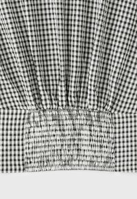 Tissu vichy noir et blanc avec un détail smocké élastique froncé au centre sur une surface plane.