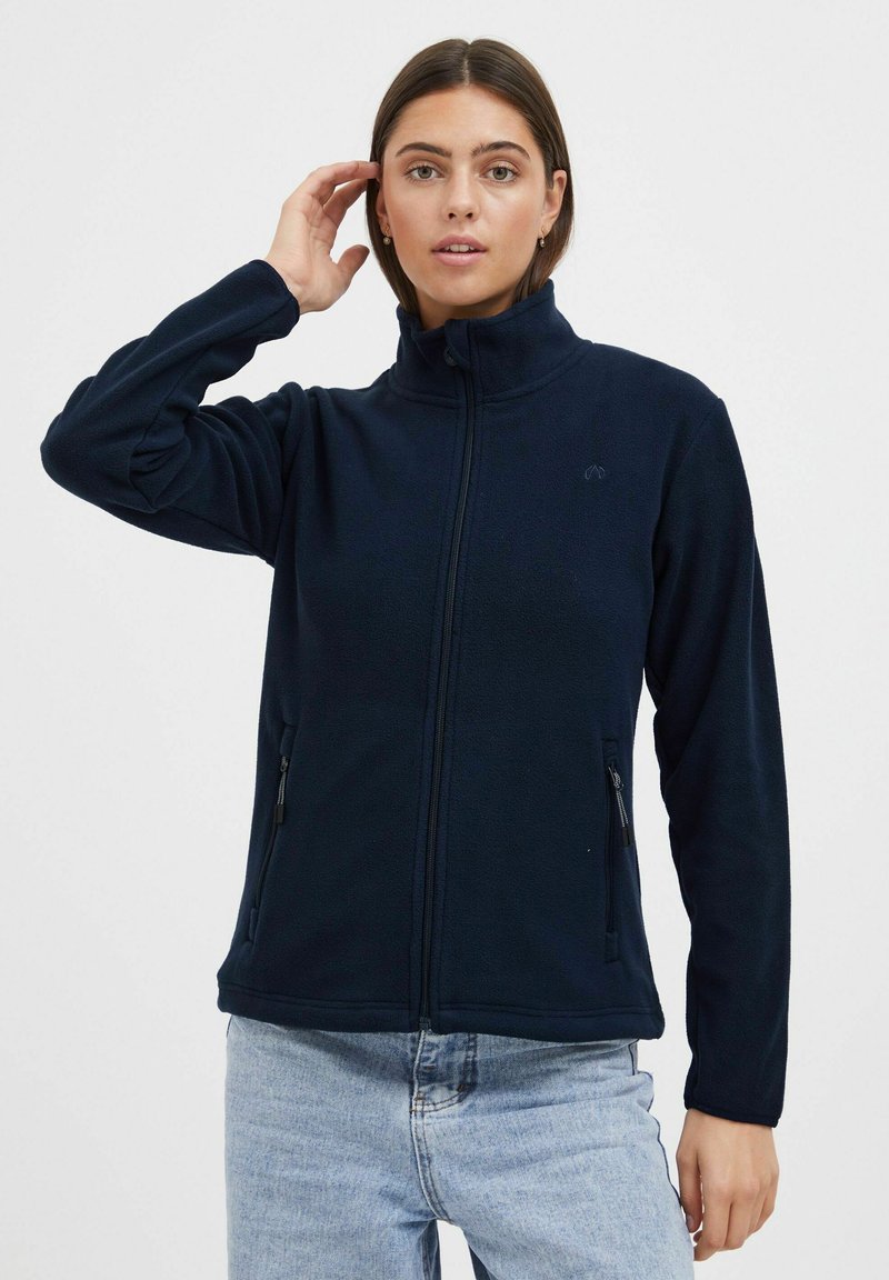 Giacca in pile blu navy con colletto alto, chiusura frontale con zip e due tasche laterali. Presenta una trama liscia e un dettaglio logo discreto.