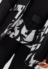 Zwarte jack met een wit en zwart abstract patroon aan de binnenkant. Het heeft zwarte hardware, drukknoopjes en een gestructureerde stofafwerking.