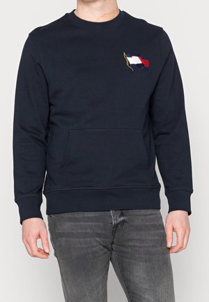 Marinblå sweatshirt med långa ärmar, rund halsringning, framficka och broderad flaggdesign i rött, vitt och blått på bröstet.