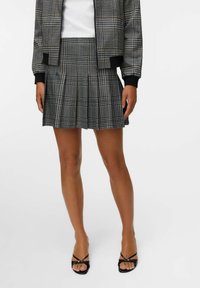 Veste bomber à carreaux noir et blanc avec des poignets et une taille à côtes, associée à une jupe plissée en tartan, portée avec des sandales noires à lanières.