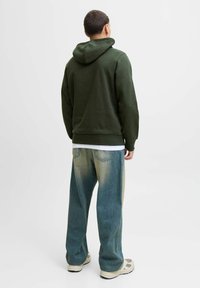 Dark green hoodie with a large hood, ribbed cuffs and hem, paired with loose light blue jeans featuring a faded effect and two back pockets.
