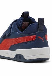 Tumesinine sneaker punaste lisanditega, valmistatud nahast ja võrkmaterjalist, kaabli ja luku sulguriga ning kummist tallaga. Omab nähtavat logo kandadel.