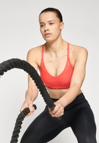 Röd idrottsbhr med justerbara remmar och logoband, kombinerad med svarta leggings. Motivet håller i tjocka, texturerade battle ropes.