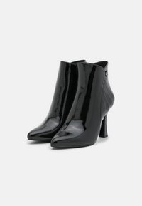 Bottines en cuir verni noir avec un bout pointu, un haut talon aiguille et un détail plissé discret à l'arrière. Fermeture éclair sur le côté.