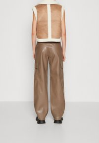 Brun shearlingväst med en krämfärgad krage, kombinerad med höga, vida bruna läderbyxor med sidofickor.