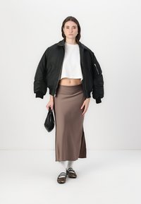 Svart bomberjakke, hvit cropped topp, brun satengskjørt, svart håndveske, hvite sokker og stripete brune sandaler med leopardmønster.