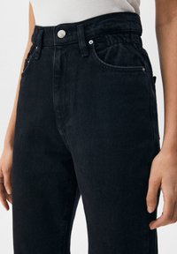 Pantalon en jean noir taille haute avec une coupe décontractée, doté de poches avant, d'une fermeture à bouton et de détails de couture subtils.