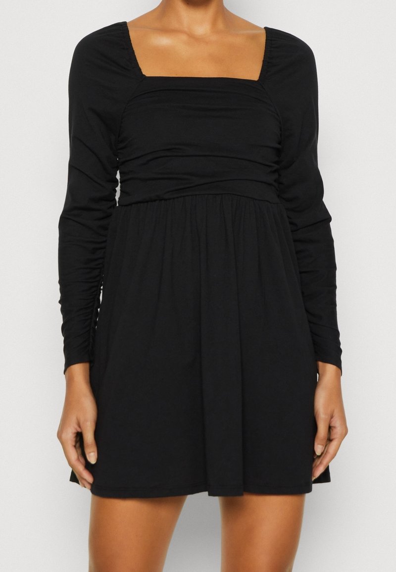 Svart långärmad klänning med fyrkantig halsringning, rynkad byst och lös midja. Tillverkad av ett mjukt tyg och har en utsvängd kjol.