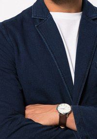 Marineblazer met gesneden revers, textielstructuur, gecombineerd met een wit t-shirt. Bruin leren polshorloge met een zilveren kast en een witte wijzerplaat.