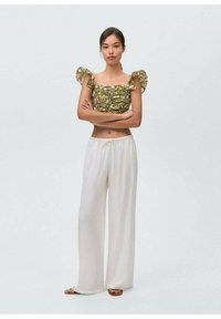 Top corto verde a fantasia con maniche a sbuffo e pantaloni bianchi svolazzanti. L'outfit presenta una vestibilità morbida e un tessuto leggero.