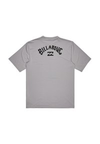 Camiseta de manga corta color gris hecha de tela suave, con un audaz logo negro de "Billabong" y un gráfico de ola en la parte posterior.
