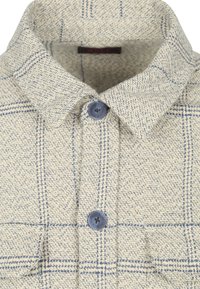 Beige en blauwe geweven stof met een kraag, voorzien van twee blauwe knopen en twee zichtbare flapzakken eronder.