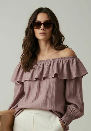 Femme portant un chemisier marron à volants et épaules dénudées, de grandes lunettes de soleil, un pantalon crème, et tenant un sac à main beige sur un fond uni.