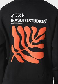 Černá mikina s oranžovým vzorem listů a bílým textem "IRASUTO STUDIOS" a "ILLUSTRATED STUDIOS" v moderním písmu.