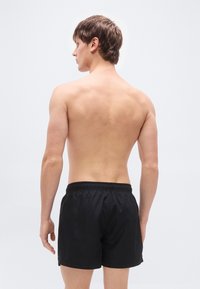 Μαύρα μαγιό σορτς με ελαστική ζώνη μέσης, μπροστινές τσέπες και άνετη εφαρμογή, παρουσιασμένα σε ανδρικό μοντέλο από πίσω.