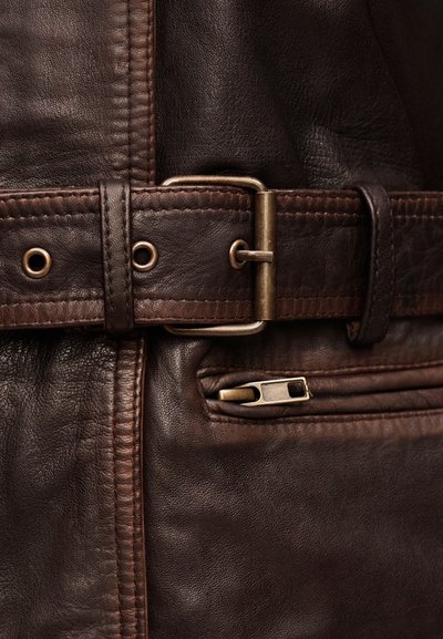 Κοντινή λήψη σκούρας καφέ δερμάτινου μπουφάν με ραμμένη ζώνη, χάλκινη αγκράφα και μερικώς φερμουαρτζέ τσέπη.