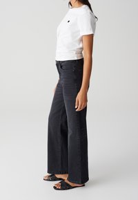 White cotton t-shirt with black heart logo, paired with high-waisted black wide-leg jeans and black strappy sandals.