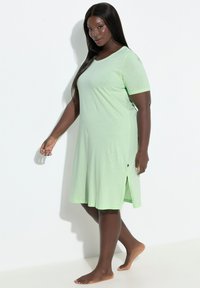 Light green short-sleeve nightdress with a round neckline, side slits, and subtle texture. Fabric appears soft and comfortable.
