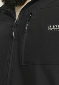 Zwarte jas met een gladde textuur, ritszakken en merktekens. Close-up weergave toont ritsen en stikdetails.