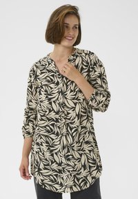 Chemise noire et beige avec un motif de feuilles, présentant une fermeture à boutons, des manches longues et un ourlet incurvé. Fabriquée dans un tissu léger.