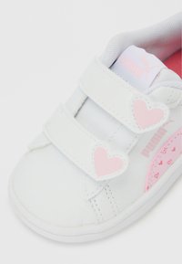 Λευκό παιδικό αθλητικό παπούτσι με ροζ καρδιόσχημες λουριά Velcro και ροζ λογότυπο Puma στο πλάι και τη γλώσσα.