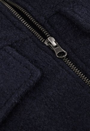 Navyblauwe stof met een textuurafwerking, voorzien van een metalen rits aan de voorkant en twee zijzakken.