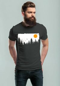 Schwarzes T-Shirt mit einem weißen und orangefarbenen Grafikdesign von Bäumen und einer Sonne vor einem hellen Hintergrund. Aus weichem Baumwollmaterial mit kurzen Ärmeln.