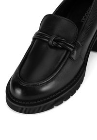 Must musta stiiliga mustad nahast loafer-tüüpi kingad, millel on dekoratiivne sõlme detail, ümar varvas ja tekstuuriga kummitald ribadega aksentidega.