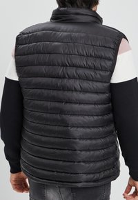 Chaleco negro acolchado con diseño de acolchado horizontal, cuello alto y estilo sin mangas. El material se ve suave y reflectante.