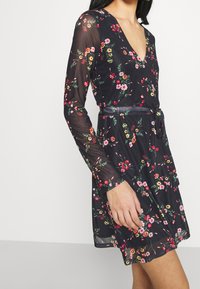 Schwarz blumiges Kleid mit langen durchsichtigen Ärmeln, V-Ausschnitt, tailliertem Schnitt und einem fließenden Rock mit roten, pinken und grünen Blumenmustern.