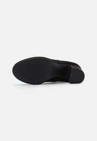 Semelle de chaussure noire présentant une surface lisse avec une texture nervurée pour l'adhérence, conçue pour la stabilité, avec une forme arrondie et un minimum de détails.